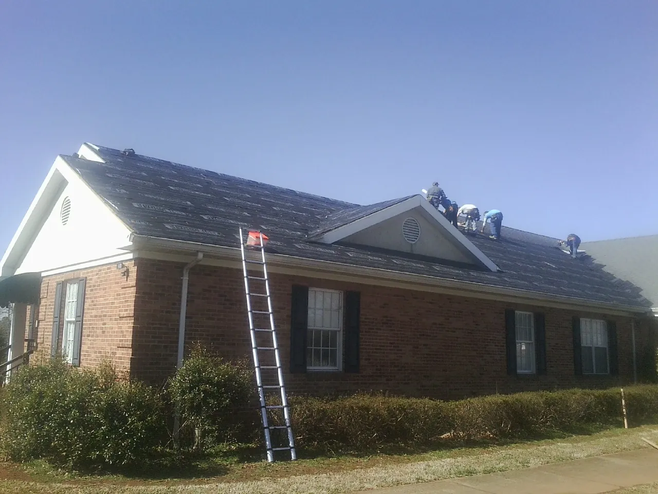 Crew tearing shingles off a brick ranch roof with a ladder set — Emergency Roof Repair work by our crew in Essex Fells