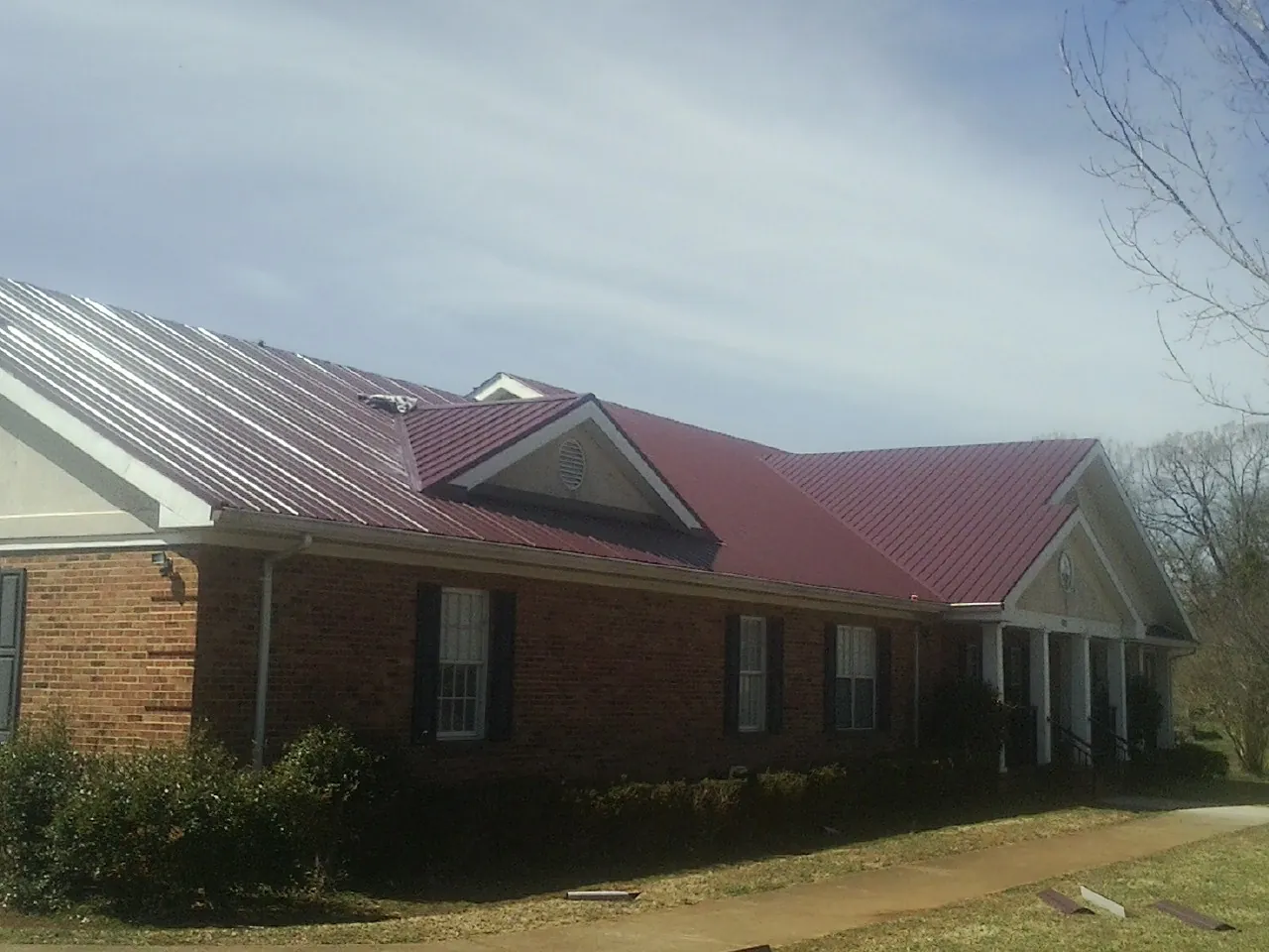 Red metal roof with gabled entries on a long brick building, from a Hail Damage Roof Repair job in Essex Fells