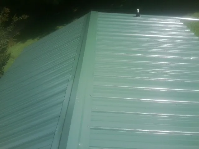 New green metal panels meeting at the ridge of a roof — Flat Roof Repair work by our crew in Essex Fells
