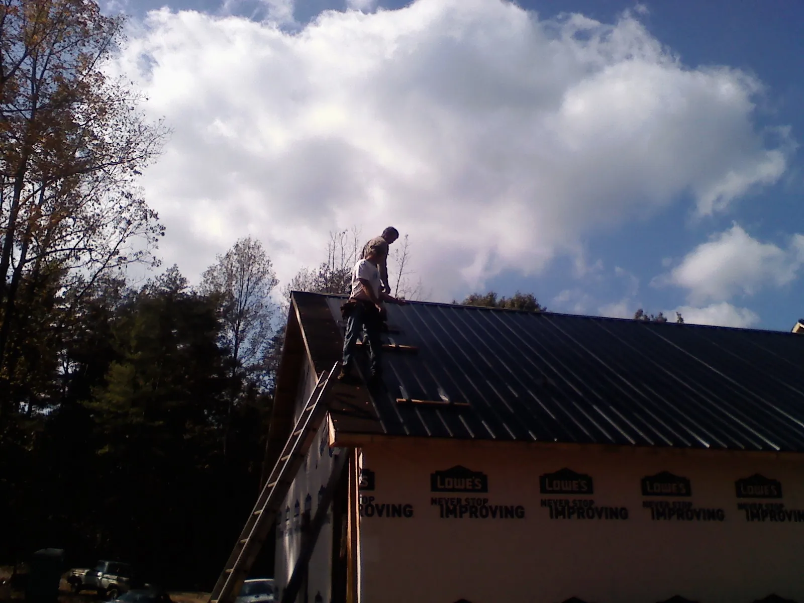Roofer fastening dark metal panels high against a cloudy sky, from a Roof Inspection job in Essex Fells