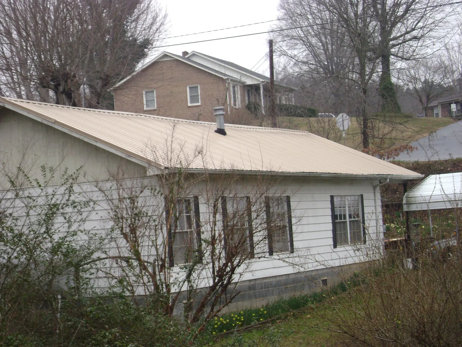 Tan metal roof on a white sided house set into a hillside — Commercial Roofing by Roofing Brothers in Essex Fells